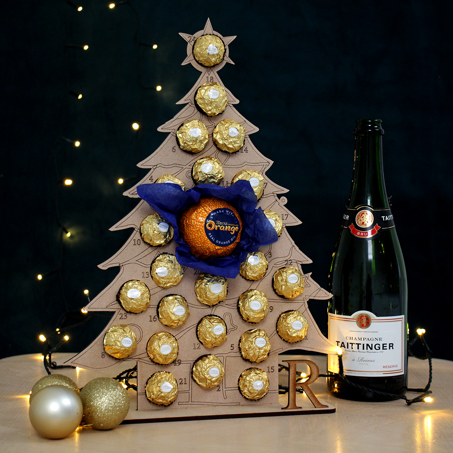 Christmas Tree shaped MDF advent calendar filled with chocolate on table in front of black background with fairy lights