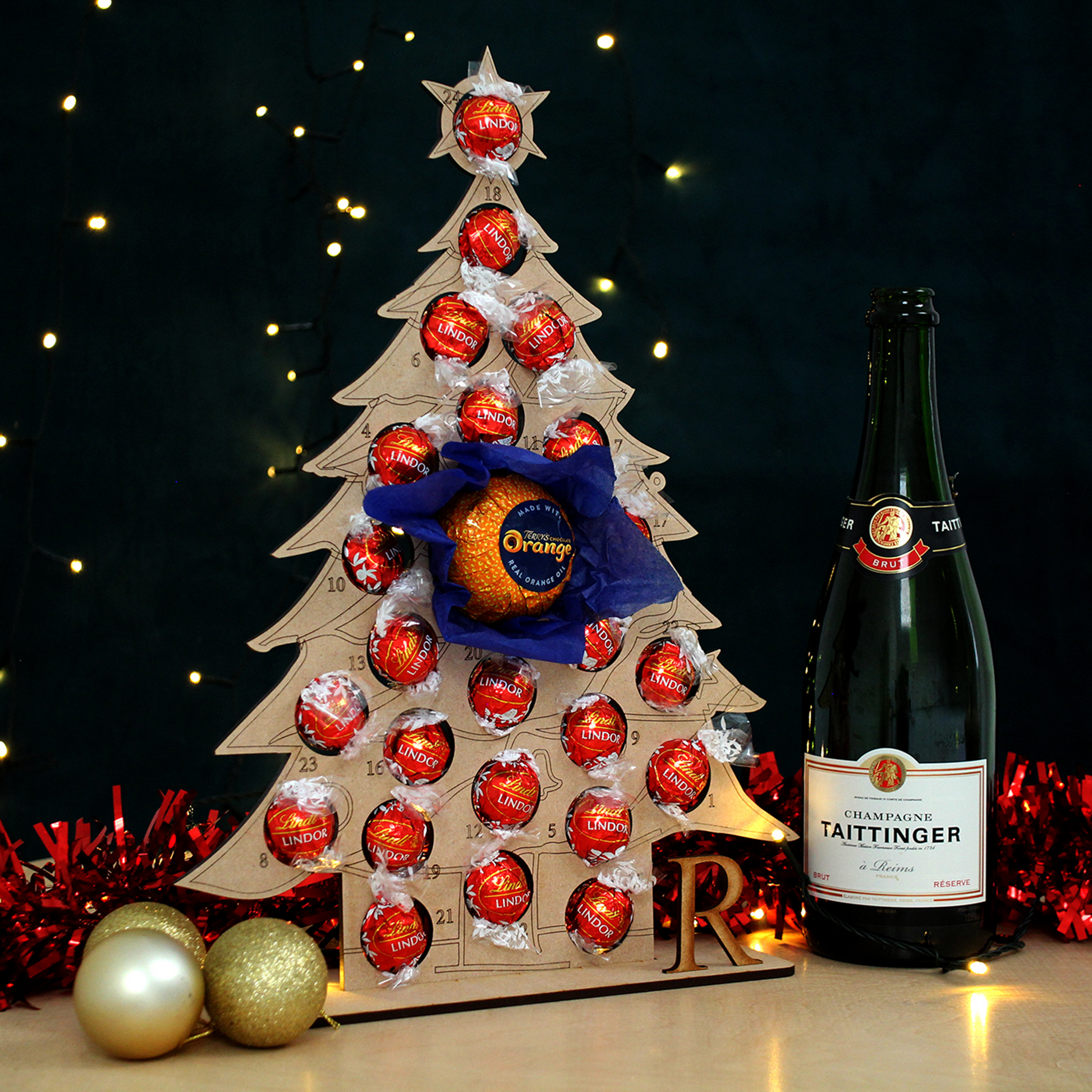 Christmas Tree shaped MDF advent calendar filled with chocolate on table in front of black background with fairy lights