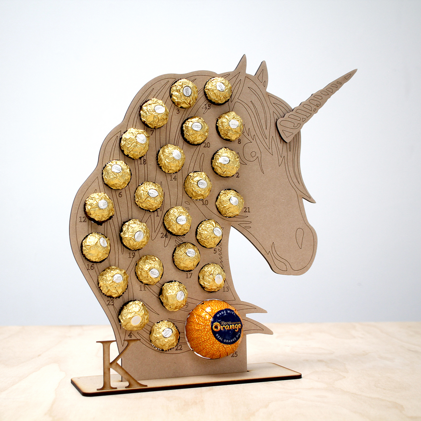 Unicorn shaped MDF advent calendar filled with chocolate on table in front of white background