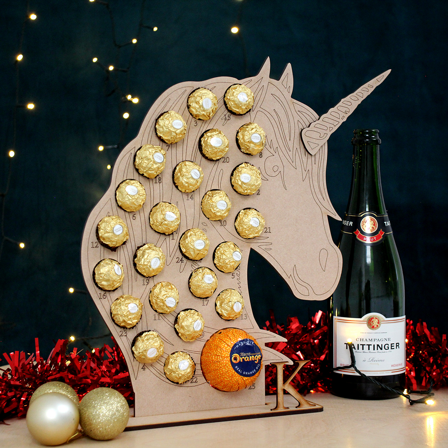 Unicorn shaped MDF advent calendar filled with chocolate on table in front of black background with fairy lights